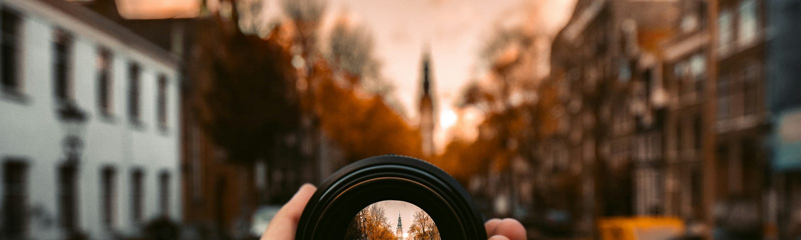 A camera lens is held in hand, focusing a picturesque view of a city river.