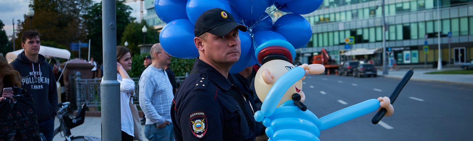 A city police officer holding a balloon police man toy while staring at the camera with a scowl.