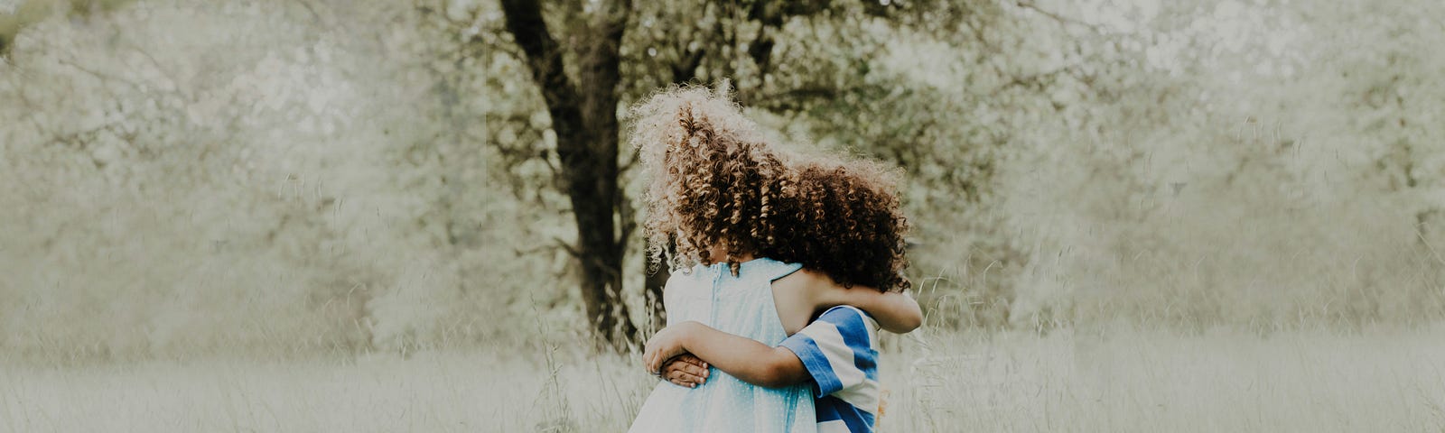 Young children hugging in a grass field.