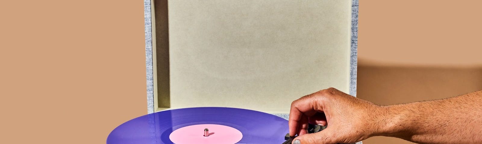 A hand putting a record player needle on a purple vinyl record