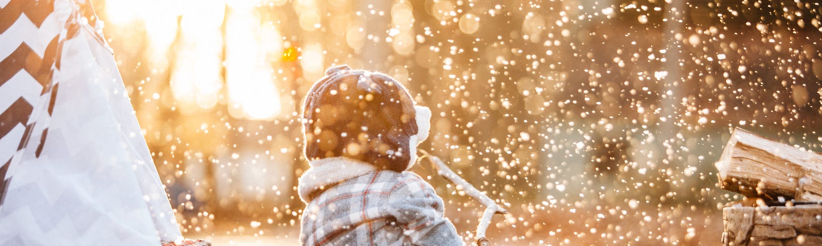 A child outside near a play tent, in golden light with glittering snow all around