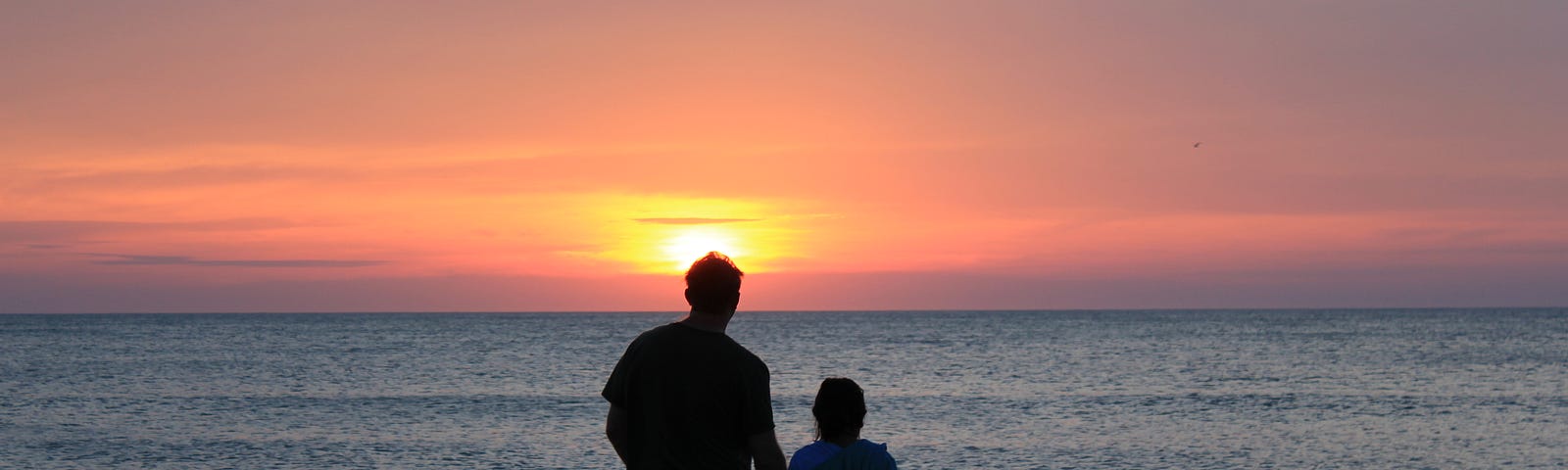 man and girl/young woman walking into a watery sunset with their backs to the camera