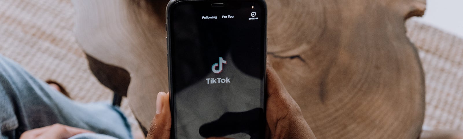 A Black person is holding an iPhone and opening up the TikTok app.