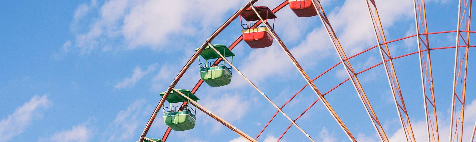 Ferris wheel with green seats and red seats, clouds in the background