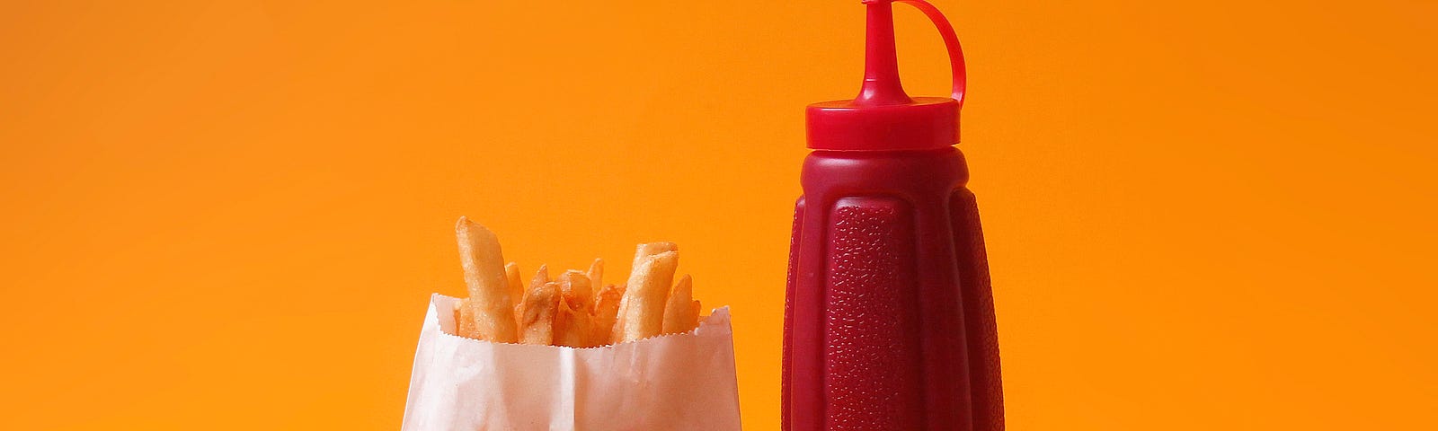 Photo of french fries in a paper wrapper on the left, and a red ketchup bottle on the right. Fast food can contain phthalates.