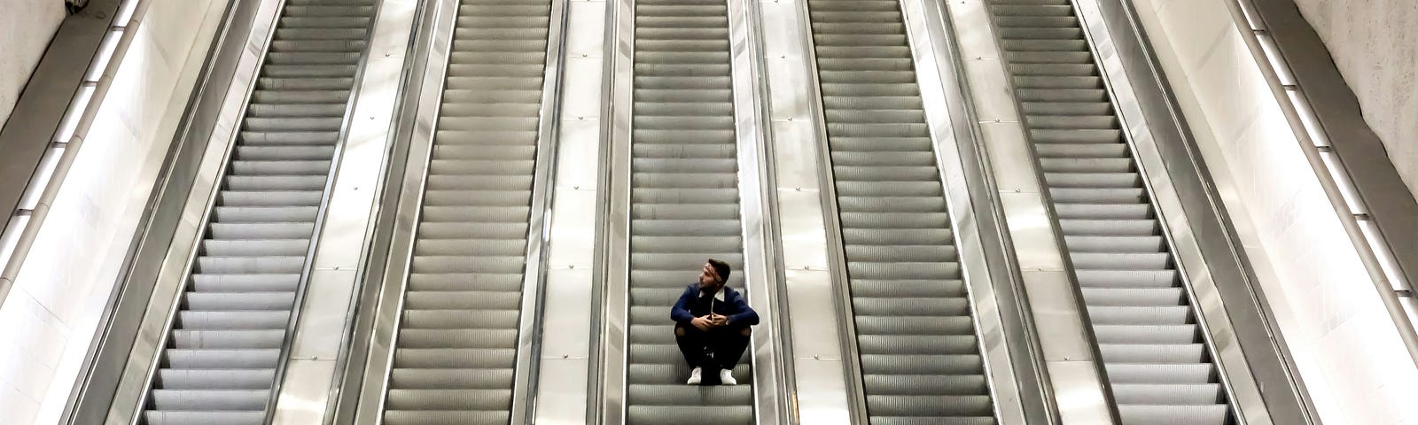 A young man sits on an empty escalator