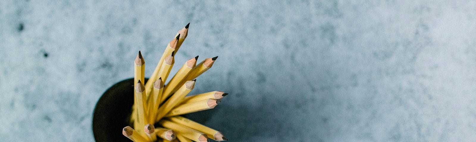 A birds eye view of a pencil pot filled with yellow pencils on a grey surface.