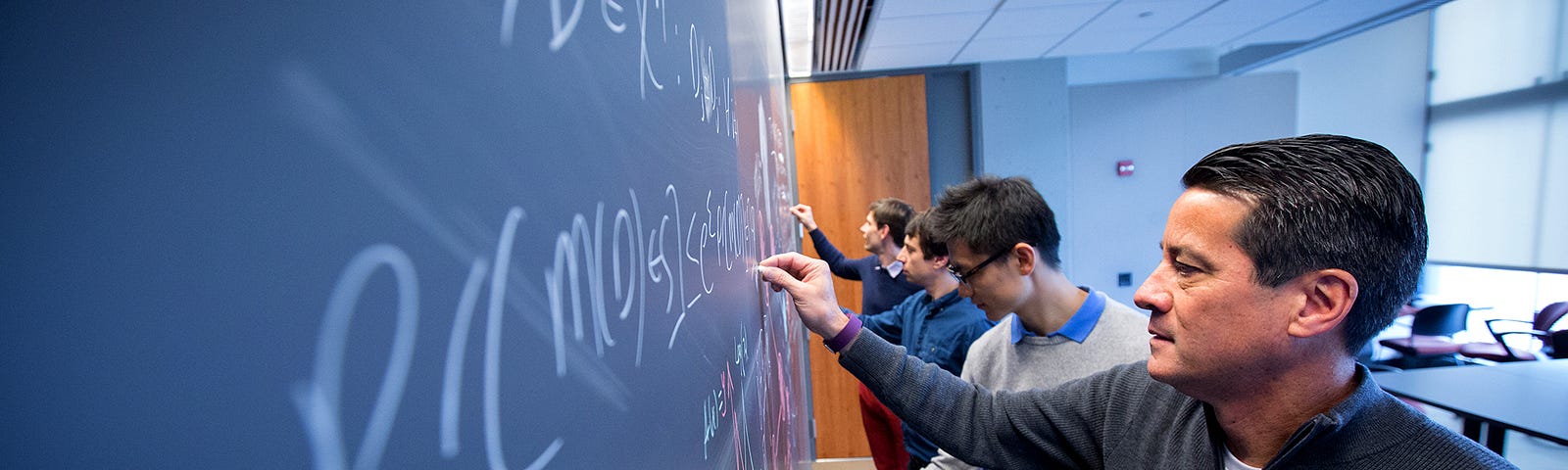 Four researchers write equations on a chalkboard.
