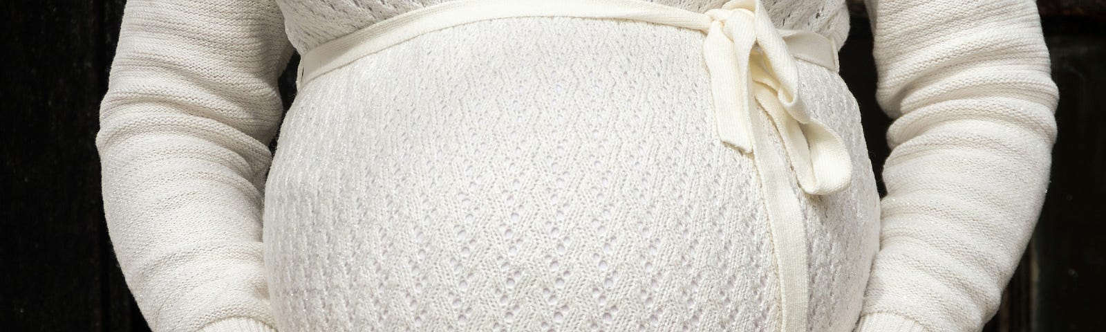Close-up of pregnant torso in a white sweater holding their baby bump. When a woman is five months pregnant with a baby girl, the cellular beginnings of all of the fetus’s eggs have developed.
