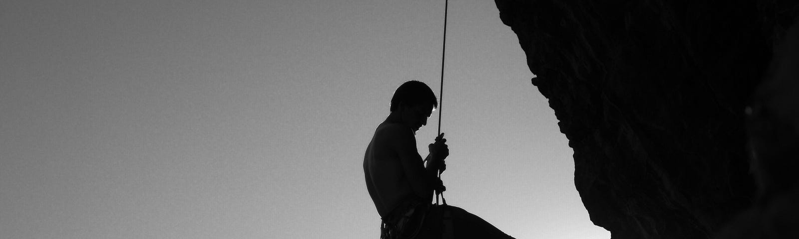 Rockclimber hanging from rope — black and white image.