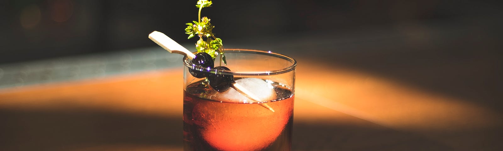 Most likely a whiskey-based cocktail with a sprig and a toothpick of olives under light