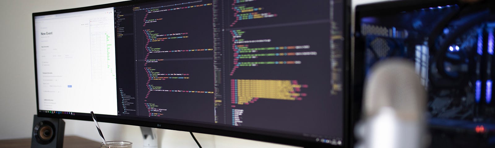 An ultra-wide monitor displaying code inside an editor alongside a cup of coffee, sits on a wooden desk.