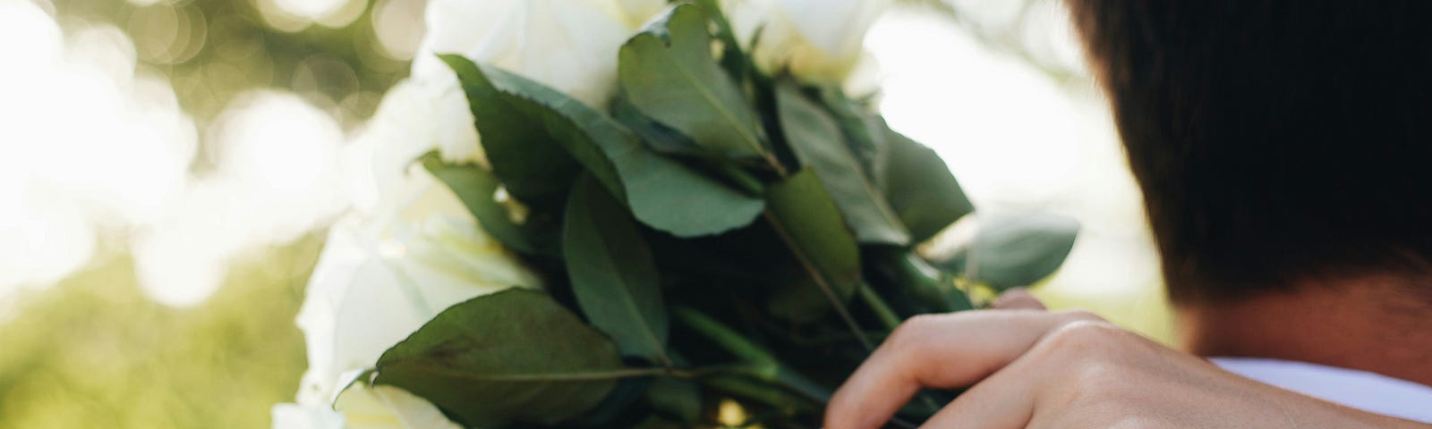 Zoomed in photo of a woman holding white flowers, a blue ring on her finger.