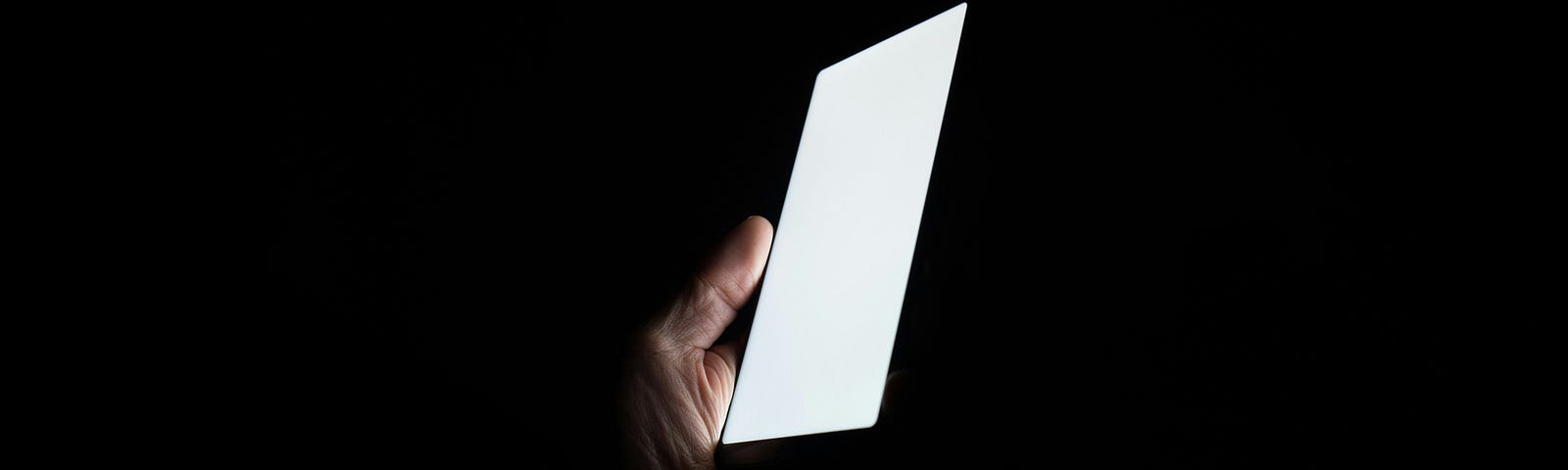 The white glow of a phone screen in a persons hand surrounded by complete darkness