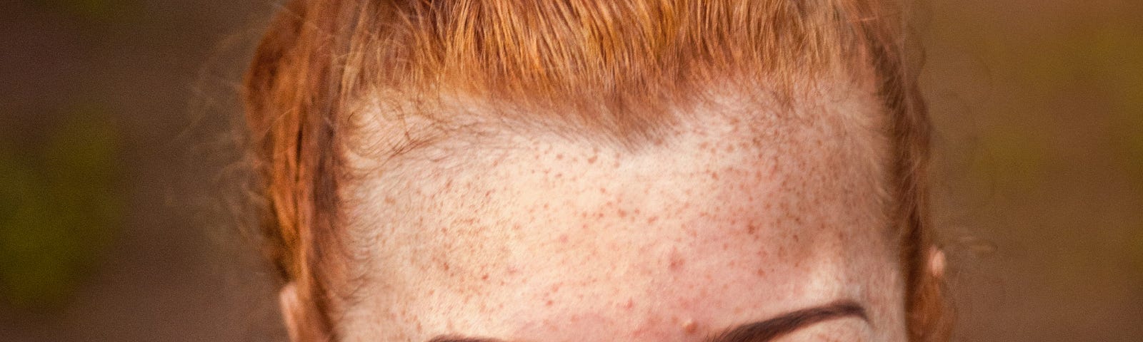 A smiling red-headed woman with red lipstick and freckles