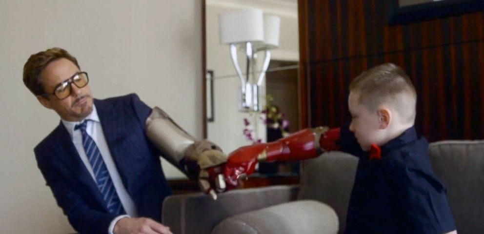 An image of Alex Pring, a 7-year-old boy with a newly-given Iron Man themed prosthetic arm, sharing a fist-bump with Robert Downey Jr., famously known for playing Tony Stark (Iron Man) in Marvel Movies.