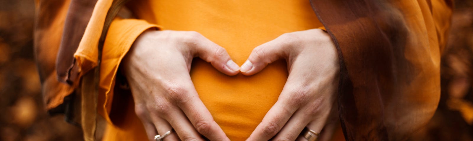 A woman holding her stomach with her hands shaped like a heart.