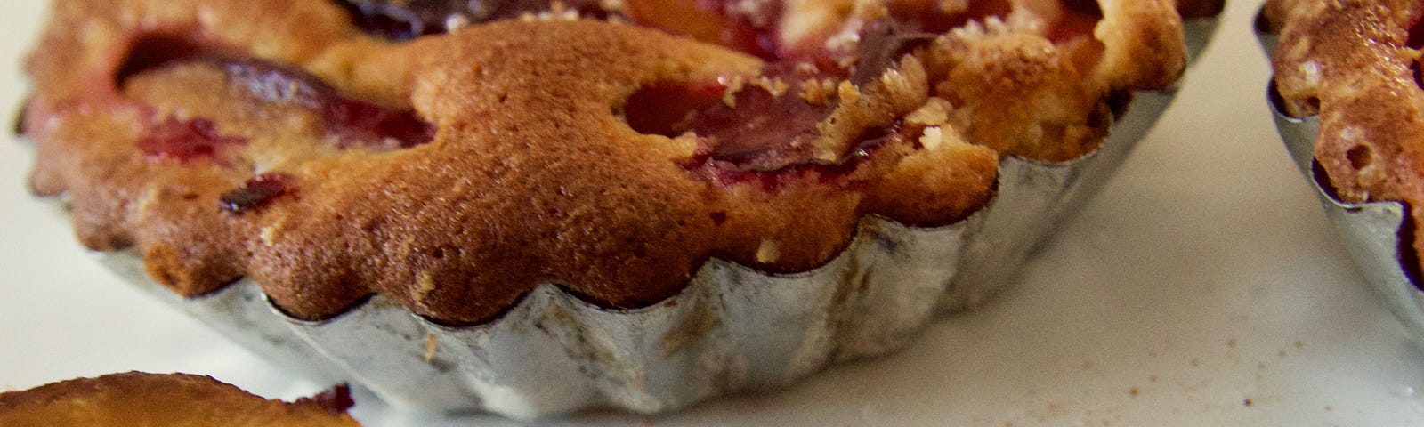 An image of a peach cobbler. On the table is an already baked pie, a half of a ripened peach and a stick of cinnamon. There is also an sprinkling of spice on the table.