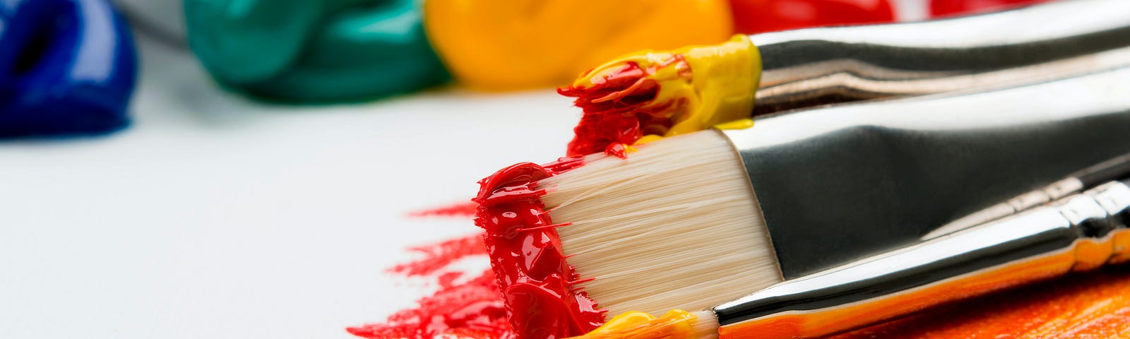 Paint brushes covered with red and yellow paint, fading together into orange.