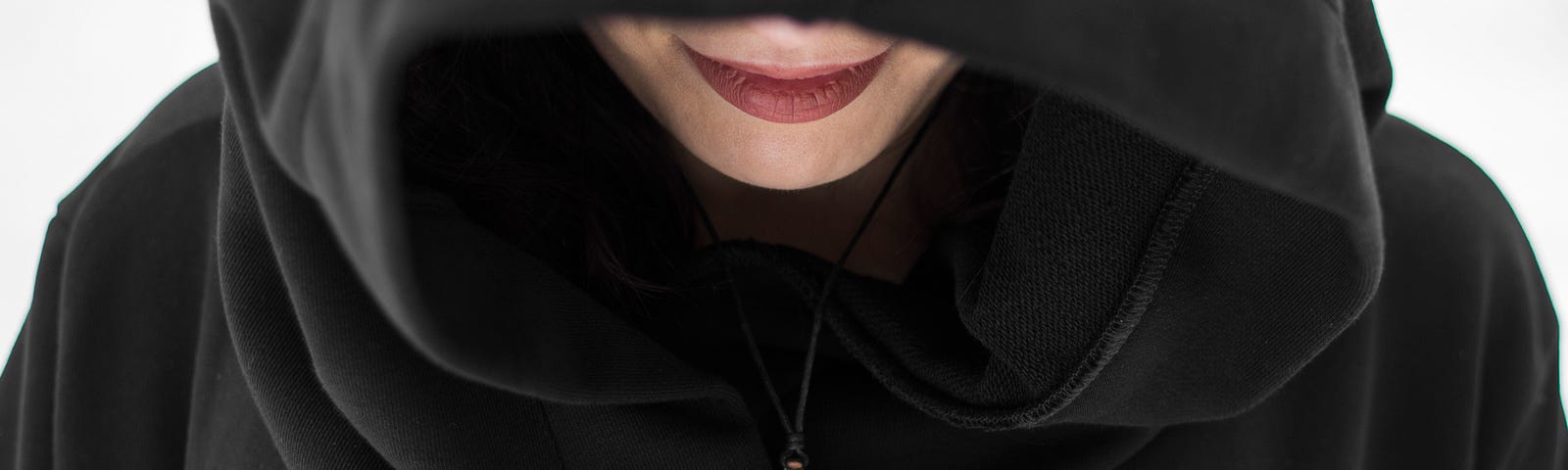 woman wearing a black cloak that covers most of her face, save for colored lips, and also wearing a magickal amulet with the moon and stars.