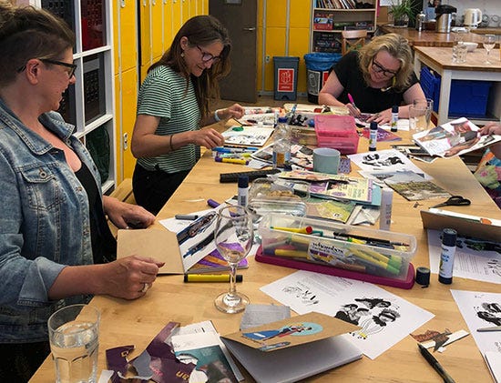 Three people sitting around a table of cut up magazines and art supplies, laughing while they work