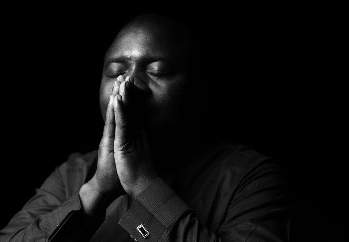 Man praying with hands clasped over mouth.