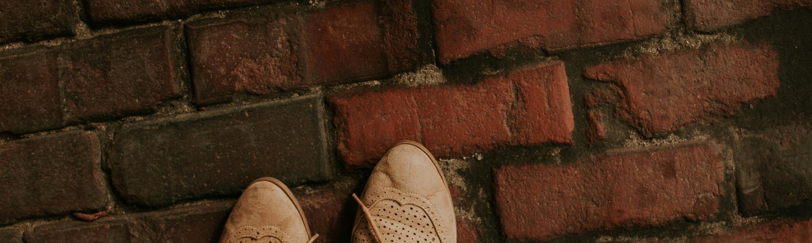 Photo of a brick floor with a person standing on it, the only thing in sight are a couple of cinamon colored leather shoes.
