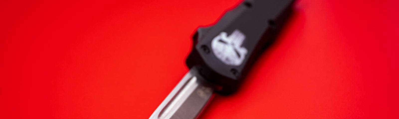 A knife with a skull on the hilt lies on a red background.