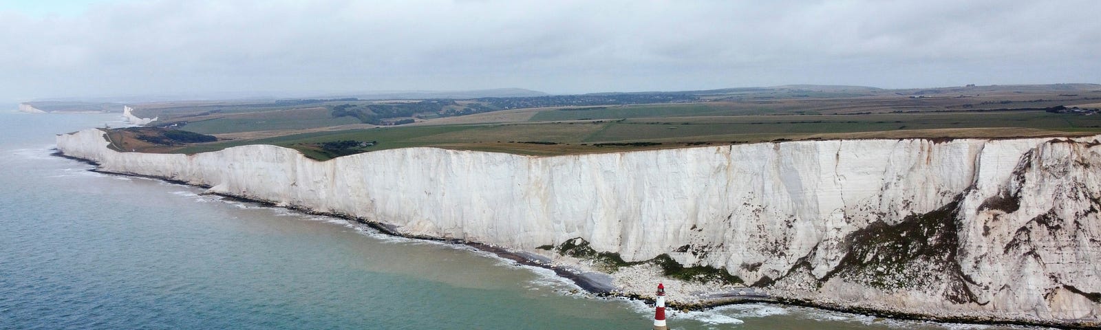 The long stretch of Beachy Head’s cliffs dwarfs the red and white lighthouse in the sea below.