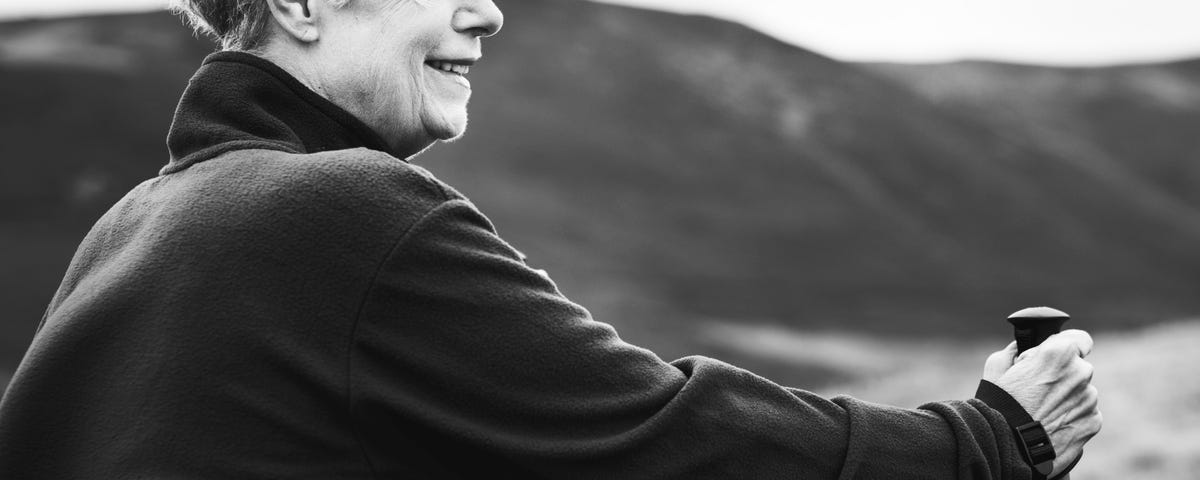 Black and white photo of a middle aged woman, smiling, with walking poles.