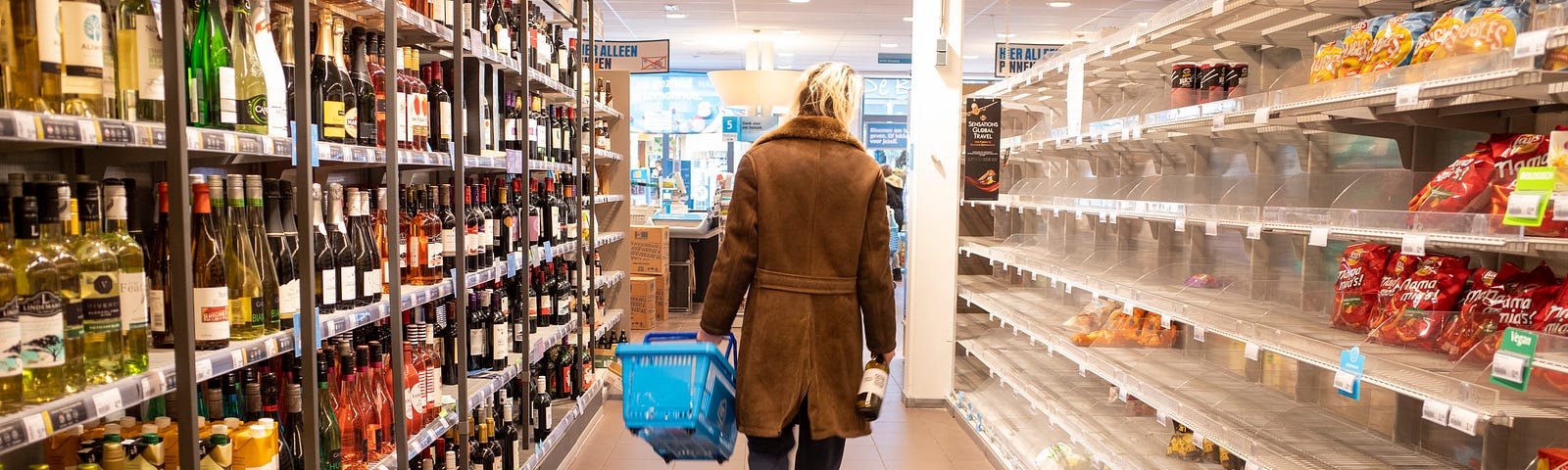 A woman walking down a grocery store aisle with a basket in hand