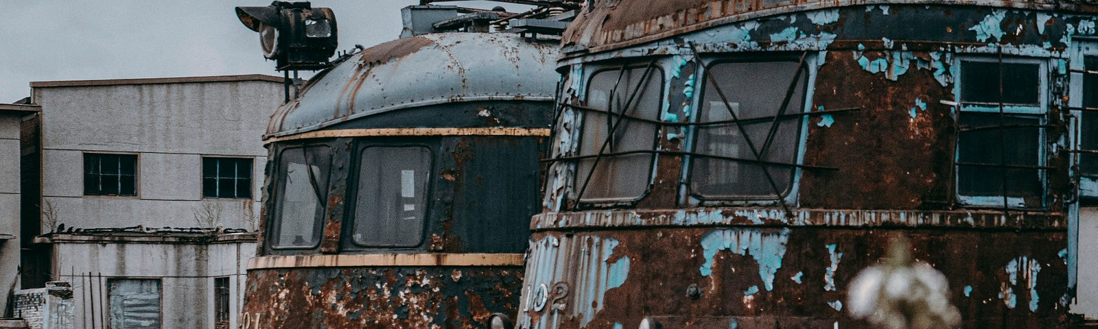Old and rusty commuter trains stand in an abandoned depot.