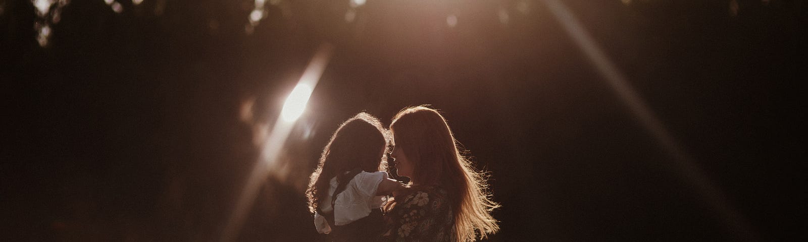 a mother holds a young daughter, backlit with sunshine