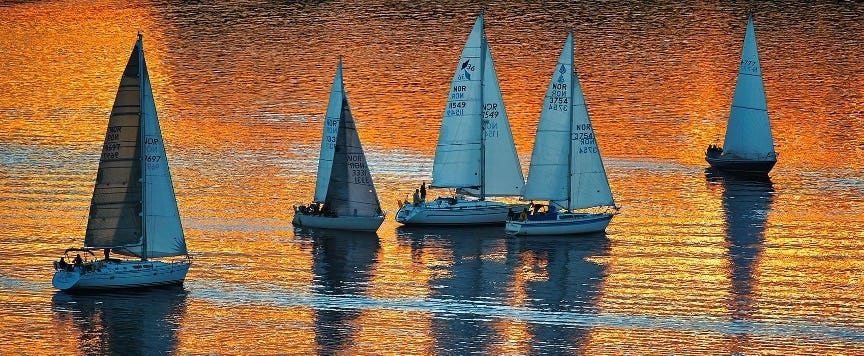 sail boats floating on water with shades of orange and yellow light shining on them