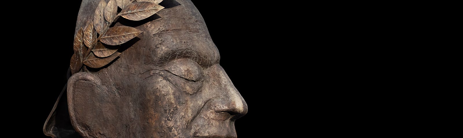 Stone sculpture of the face and neck of Julius Caesar, seen in profile. Black background.