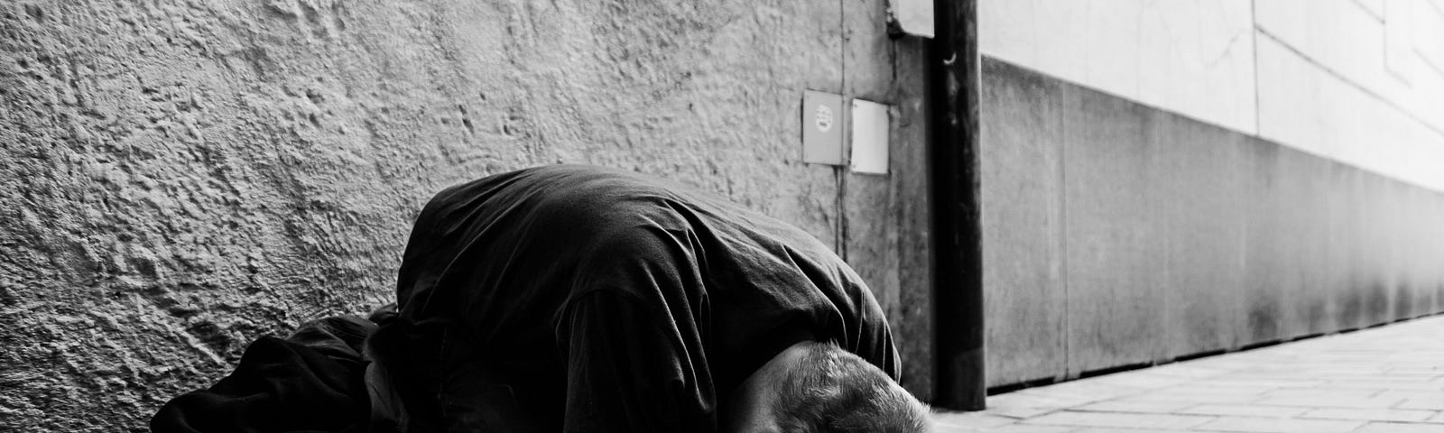 Gray image of a beggar lying on the concrete, face down.