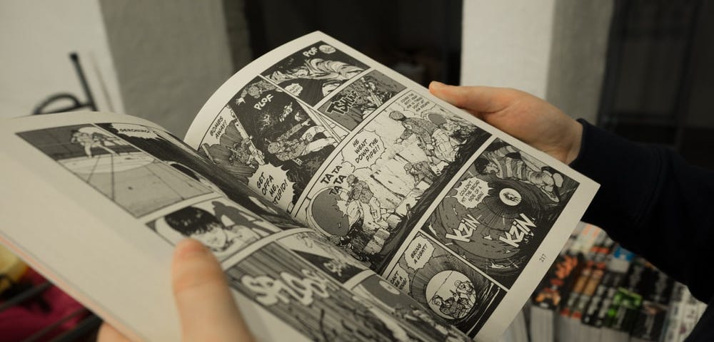 a manga novel is being held open. the pages display black and white images full of action and dialogue.