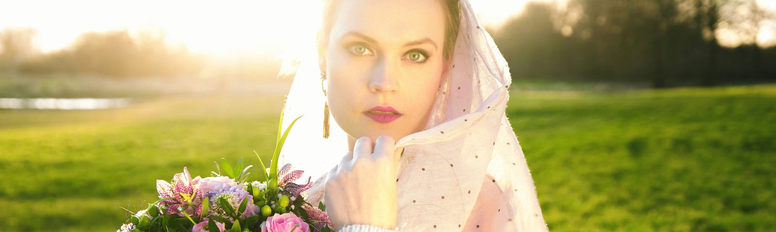 A beautiful bride in a green pasture holding a giant bouquet of flowers. This is the happiest day of her life.