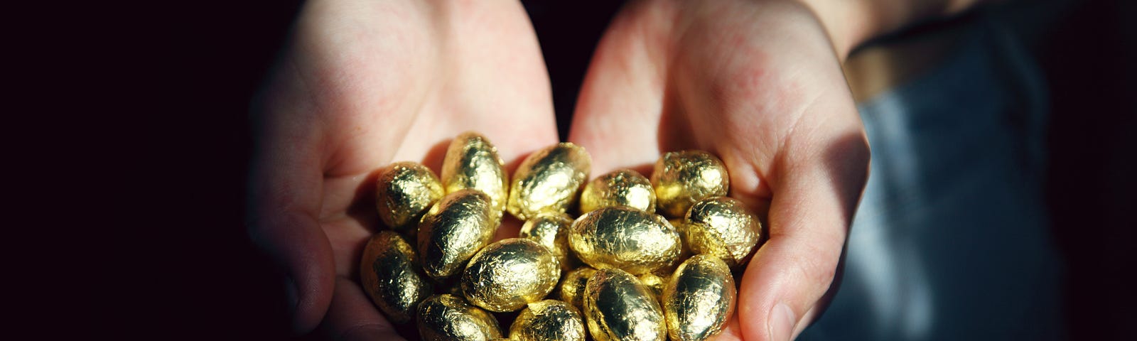 Two cupped handfuls of gold-wrapped chocolate eggs as if holding golden eggs.