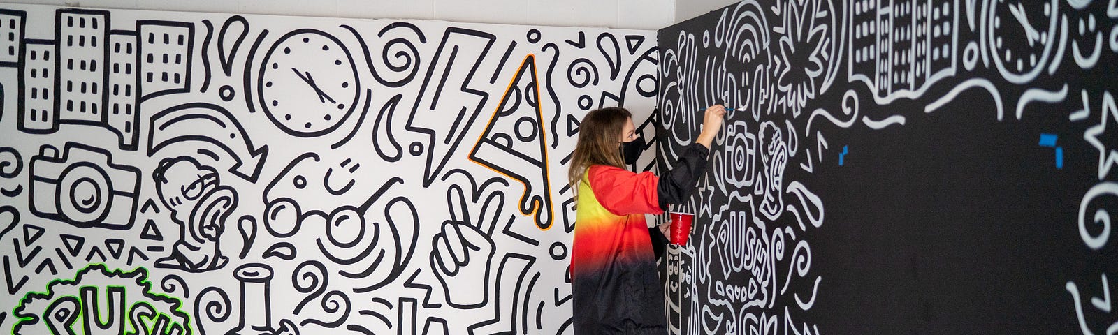 An artist standing up to a step stool and filling in a large mural on a wall.