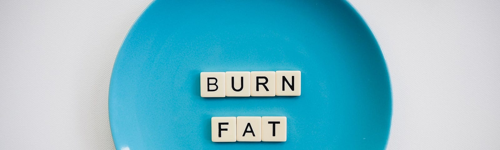 Round blue plate with tiles spelling out BURN FAT (in capital letters) on it. White/gray background.