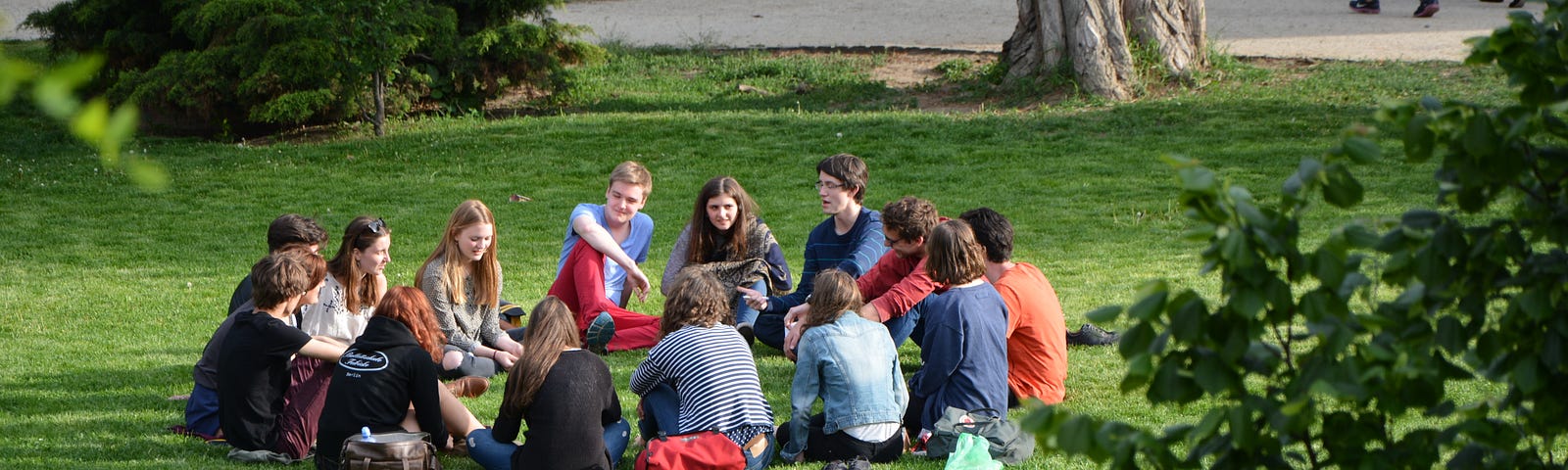 A group of about 14 people sit outside on bright green grass.
