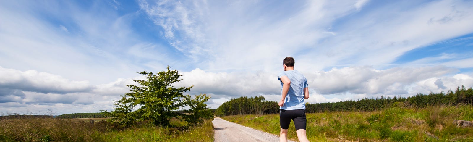 runner on gravel road under blue sky and green fields.