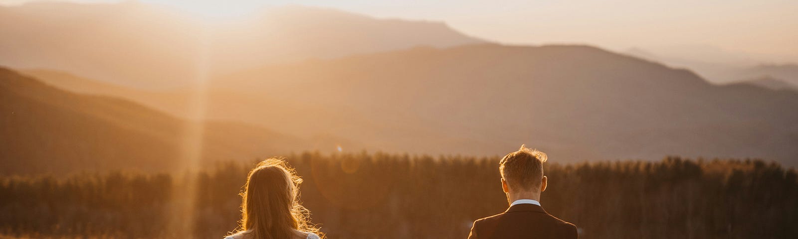 A groom leads a bride by the hand across a field at sunset.