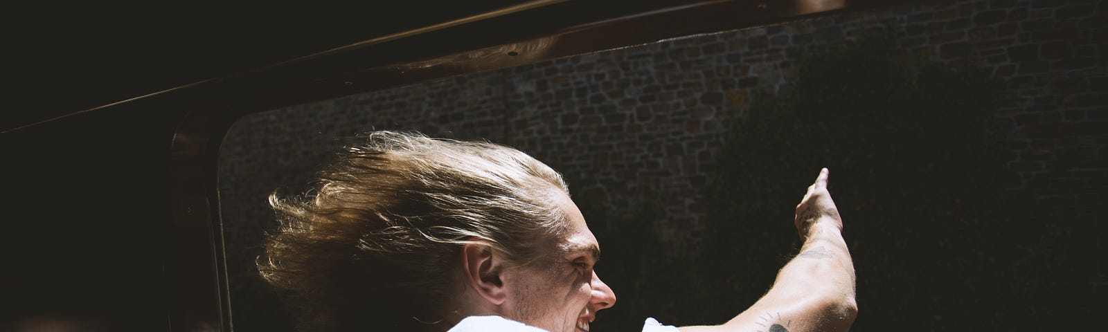 Farang lands in Bangkok. Person in white inside a vehicle, hair blowing, looking out the window and waving. Black background.