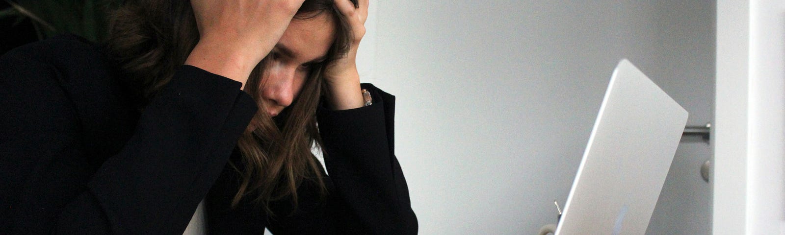 A woman sitting at a desk in front of a laptop with her head in her hands.