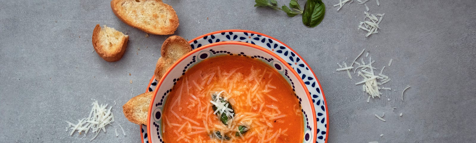 Looking down on a  bowl of minestrone soup with croutons and grated cheese sprinkled around the bowl.