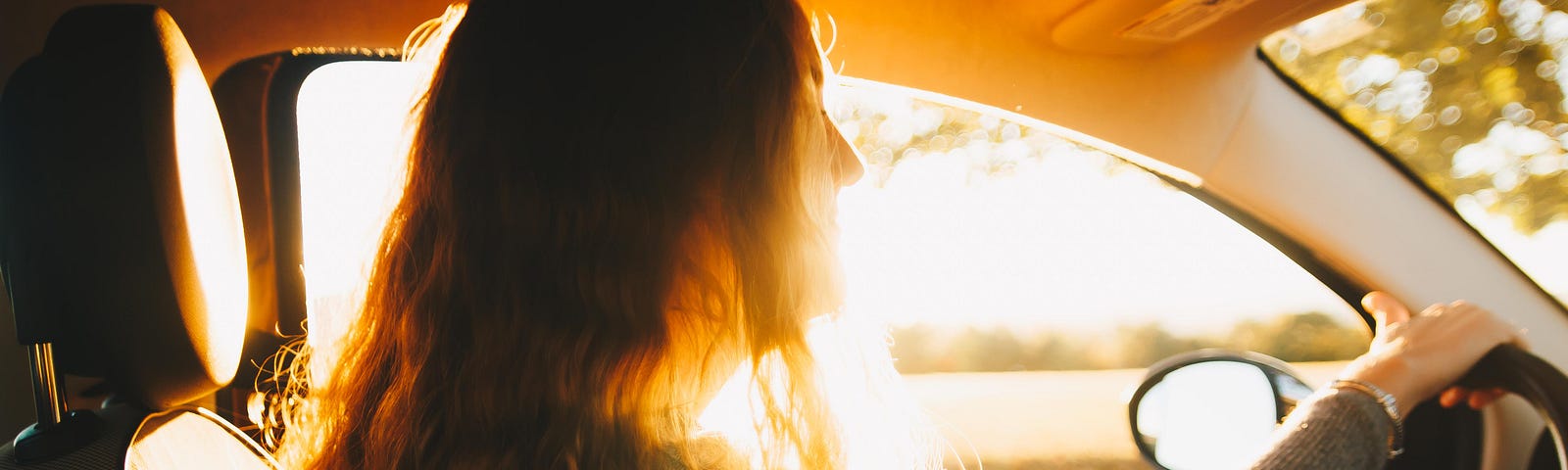 Golden light framing a long haired girl at the wheel of a car