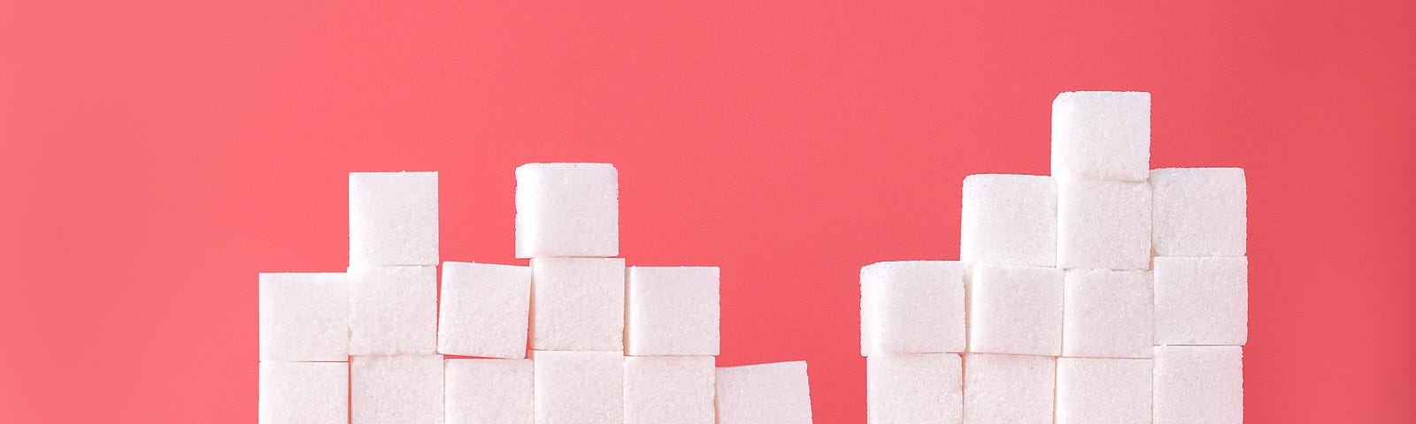 Dozens of sugar cubes are stacked up. Pink background.