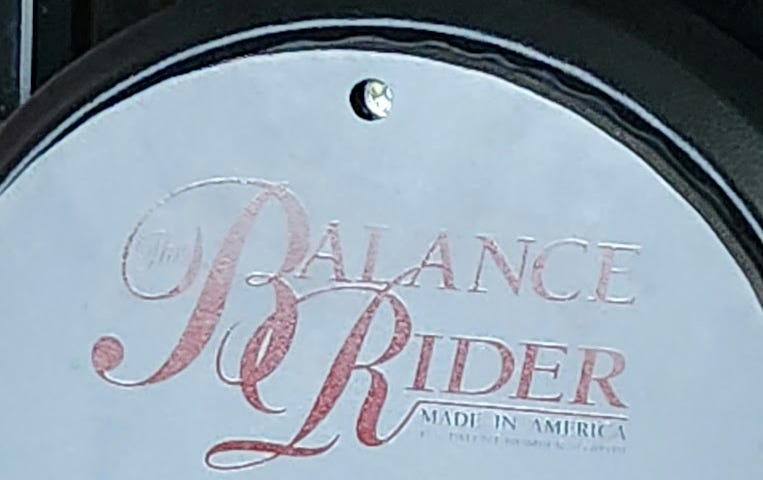 A half barrel with a black seat cover says, The Balance Rider, Made in America, on it.